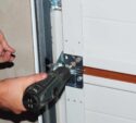 A person uses a power drill to secure a metal bracket on a white garage door.