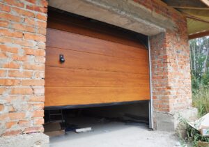 Partially open wooden garage door on a brick garage under construction, with building materials scattered on the unfinished concrete floor.