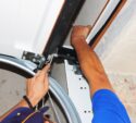 Person installing or repairing a garage door mechanism, using tools to adjust components near the door’s top corner.