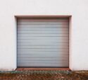 A closed gray garage door set in a white wall, with a cobblestone driveway in front.