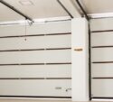 A clean, empty garage with closed white sectional doors, horizontal brown trim, and a red pull cord hanging from the ceiling.