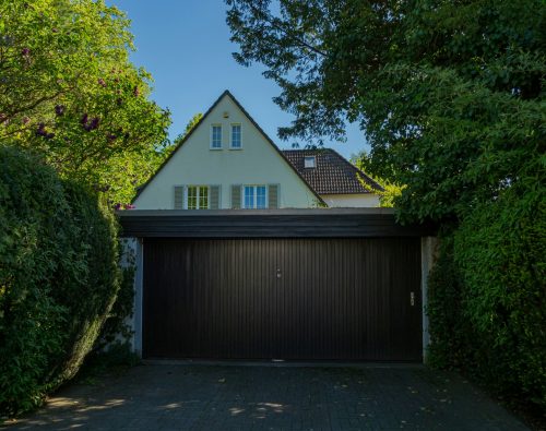 Wide dark garage door on a home framed by tall hedges