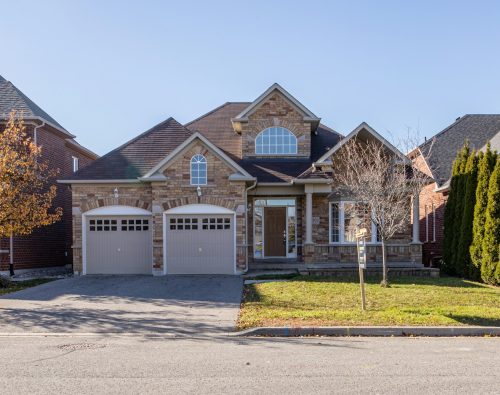 Stone home with two garage doors framed by a golden autumn tree
