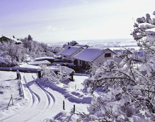 Snow covered homes and a snowy driveway with tyre tracks on a bright winter day